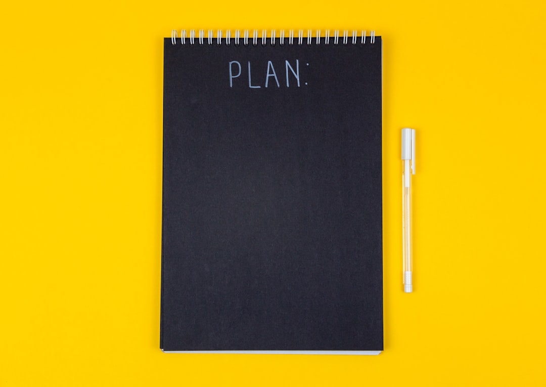Wide view image of blank black spiral note pad and white marker with calligraphic inscription plan on yellow background by Party Plan Checklist a black rectangular device